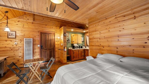 Quarto de cabana de madeira com cama, mesa de jantar e cozinha compacta.