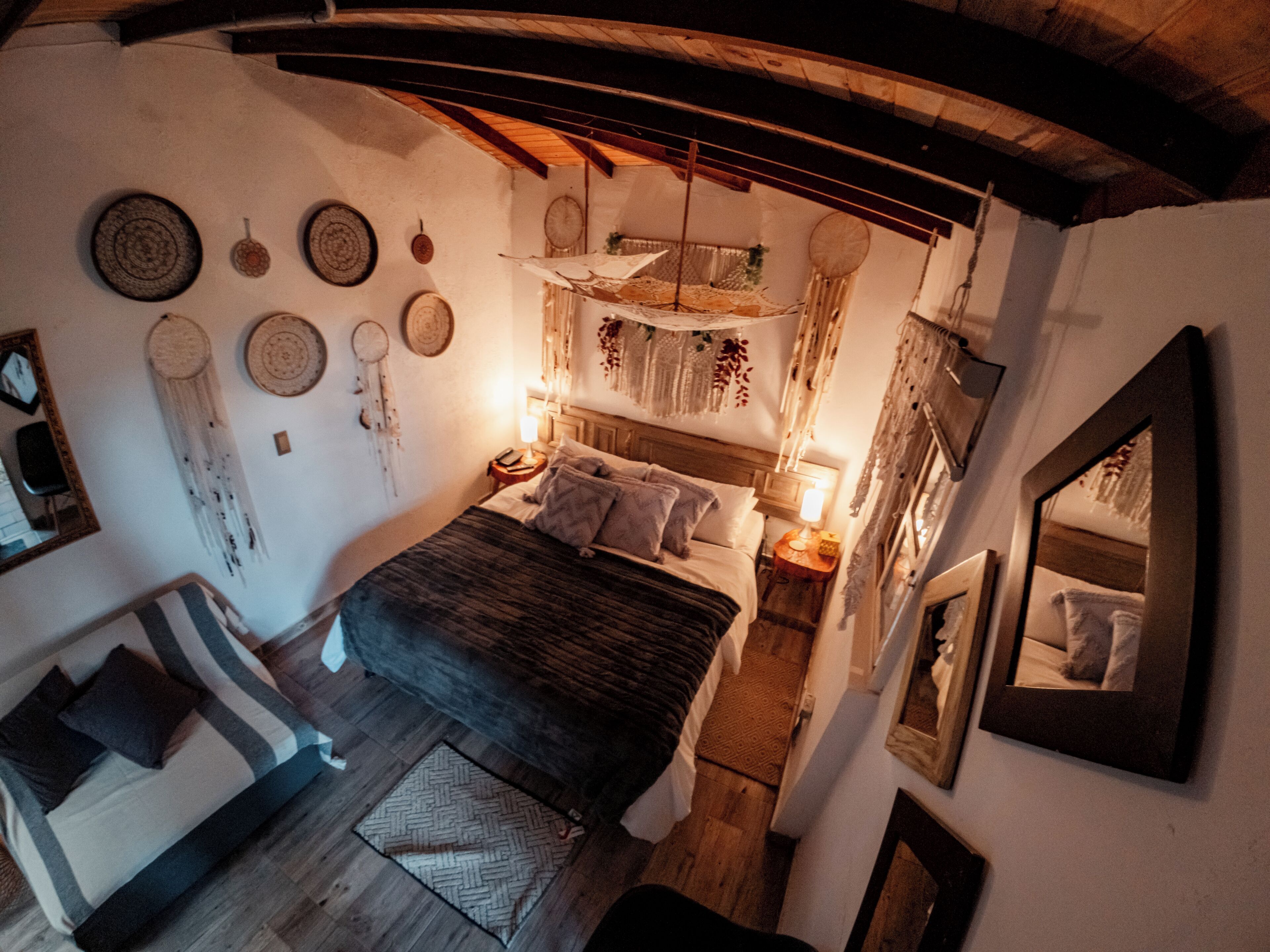 A cozy bedroom with a large bed, a small sofa, and a mirror.