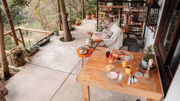 A wooden table set with breakfast items, surrounded by potted plants and a rustic outdoor setting.