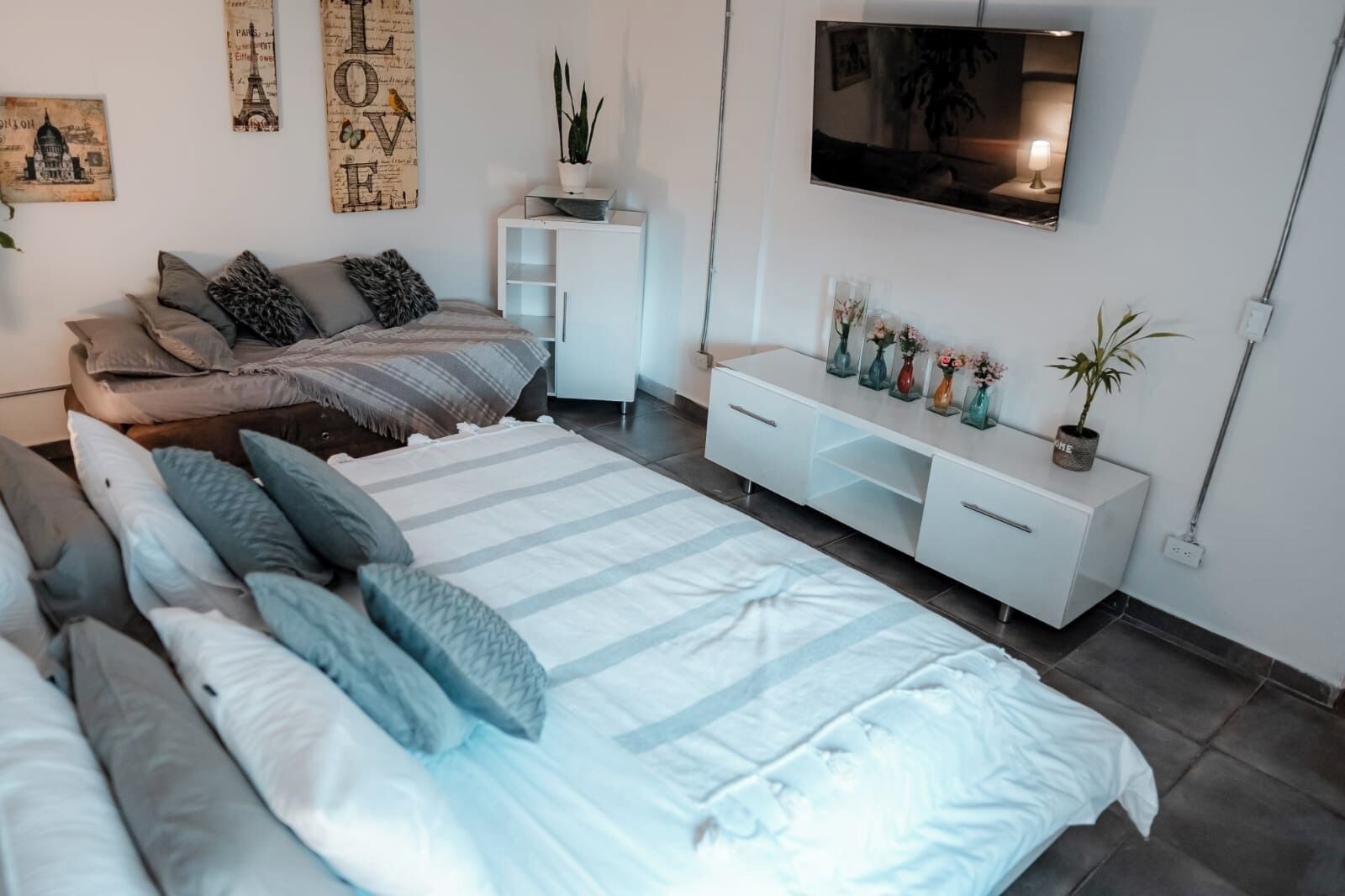 A modern bedroom with a large bed, a sofa, a TV, and a white console table with decorative items.