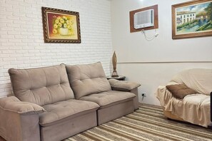 A beige sectional sofa against a white brick wall, a framed painting of flowers, and a framed landscape painting. - Enseada Beach, Guarujá - For 10 people (Guarujá)