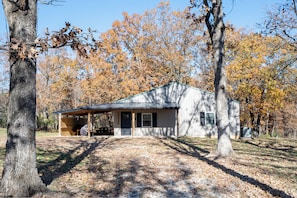 A single-story building with a covered porch, surrounded by trees with autumn foliage. - Peaceful, NEWLY Constructed Barndominium Retreat Near Fort Leonard Wood (Waynesville)