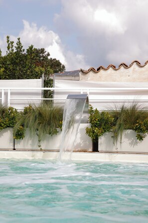 A waterfall feature in a pool with a white fence and greenery. - Dama Luxury Apartment (Pompei)