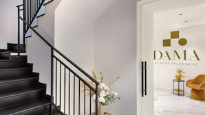 A modern staircase with black railings leading to a room with a white wall and a sign reading "DAMA LUXURY APARTMENT". - Dama Luxury Apartment (Pompei)
