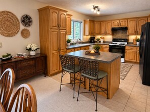 Una cocina con armarios de madera, una isla central con sillas, una estufa y un refrigerador.