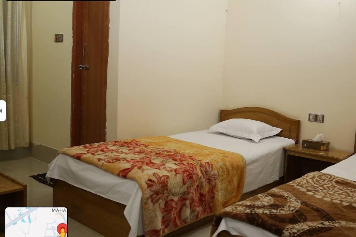 A hotel room with two single beds, each with a wooden headboard and white bedding. There is a nightstand with a lamp and a tissue box on one side.