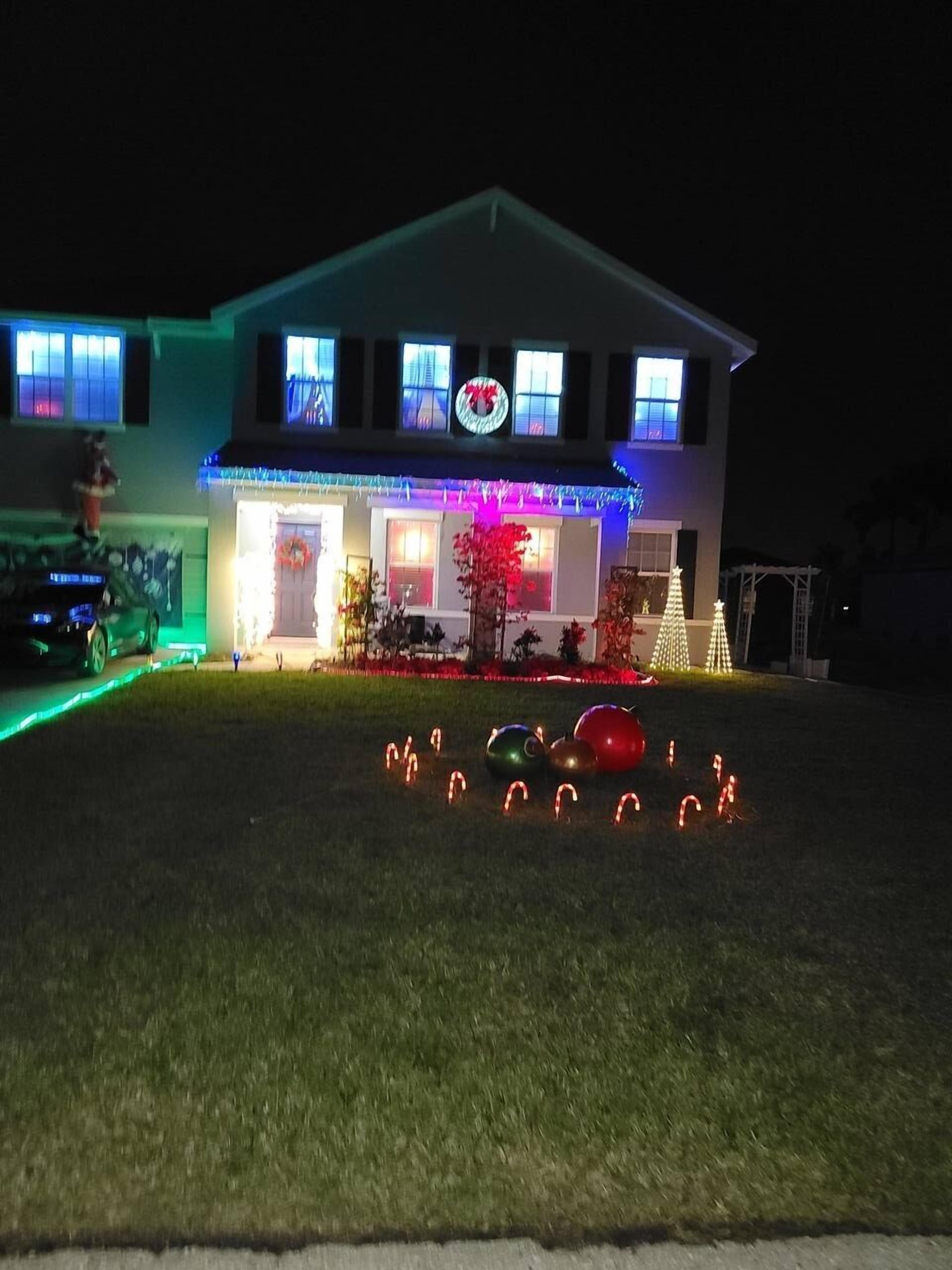 Une maison à deux étages avec un porche à l’avant, des guirlandes de Noël et une pelouse décorée de bâtons de sucre.