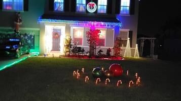 Une maison à deux étages avec un porche à l’avant, des guirlandes de Noël et une pelouse décorée de bâtons de sucre.