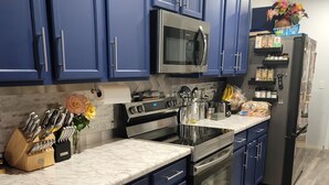 A modern kitchen with blue cabinets, stainless steel appliances, and a marble countertop.