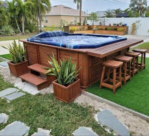 A hot tub with wooden steps and bar stools, surrounded by potted plants and a grassy area. - TR's Bed & Breakfast (Cape Coral)