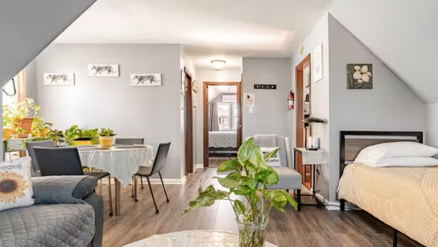A compact bedroom with a bed, a desk, and a chair. There is a dining area with a table and chairs.