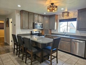 A kitchen with dark wooden cabinets, a stainless steel refrigerator, a microwave, and a large island with chairs. - Summer and Winter Getaway (Sandy)