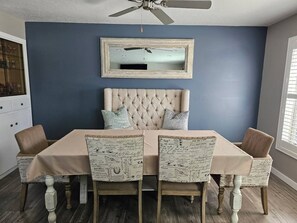 A dining area with a tufted headboard, a ceiling fan, and a table with a tablecloth. - Summer and Winter Getaway (Sandy)