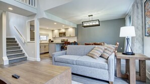 Ein großzügiger Wohnbereich mit grauem Sofa, Holztisch und einer Treppe, die zu einer oberen Ebene führt.