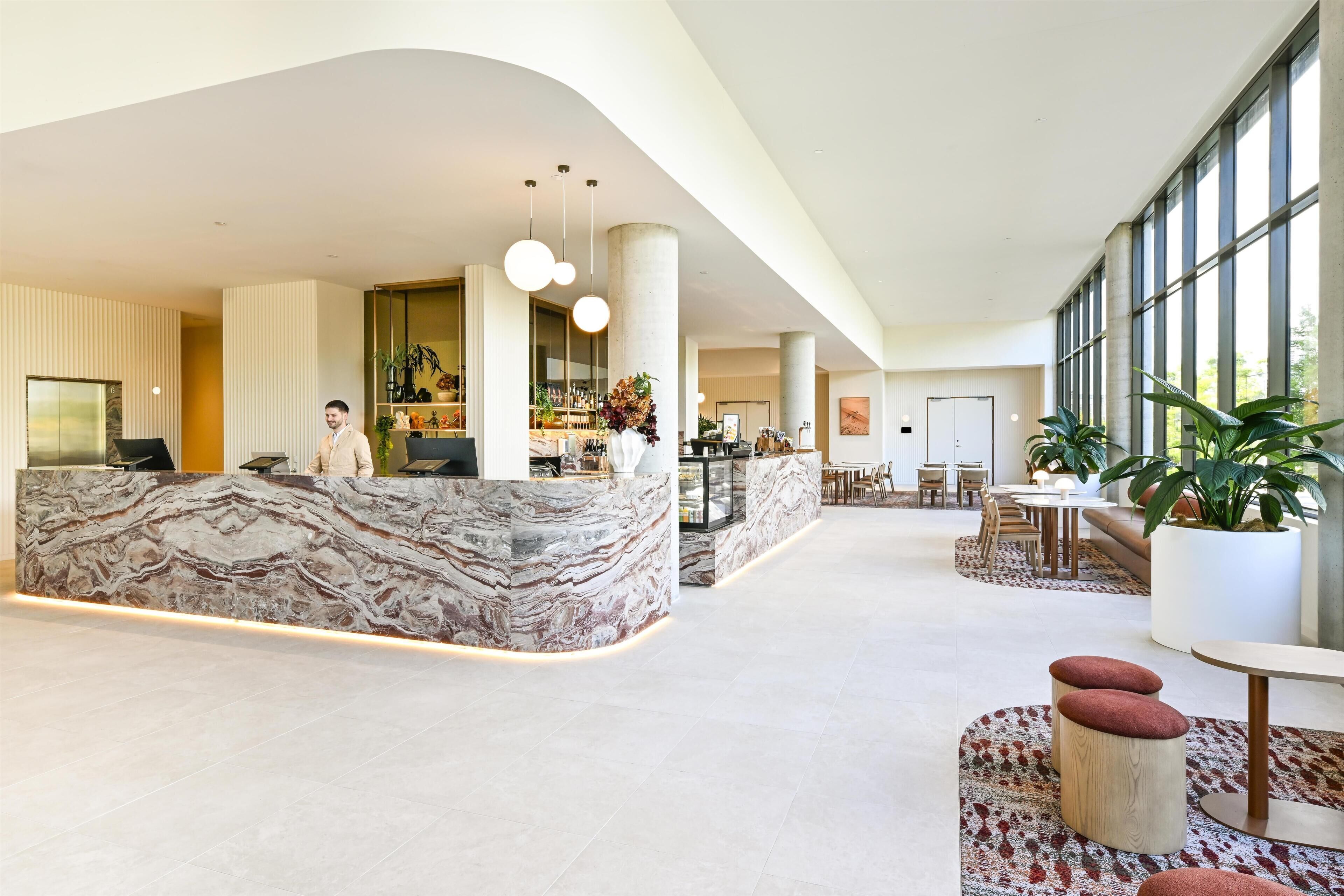 Un hall d’entrée spacieux avec un comptoir de réception en marbre, des coins salon et de grandes fenêtres.