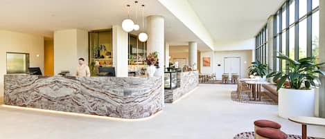 A spacious lobby with a marble reception desk, seating areas, and large windows.