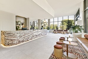 A spacious lobby with a marble reception desk, seating areas, and large windows offering views of the outdoors. - Adina Chermside Brisbane (Brisbane)