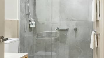 A modern bathroom with a glass-enclosed shower, a white toilet, and a wooden vanity with a shelf.