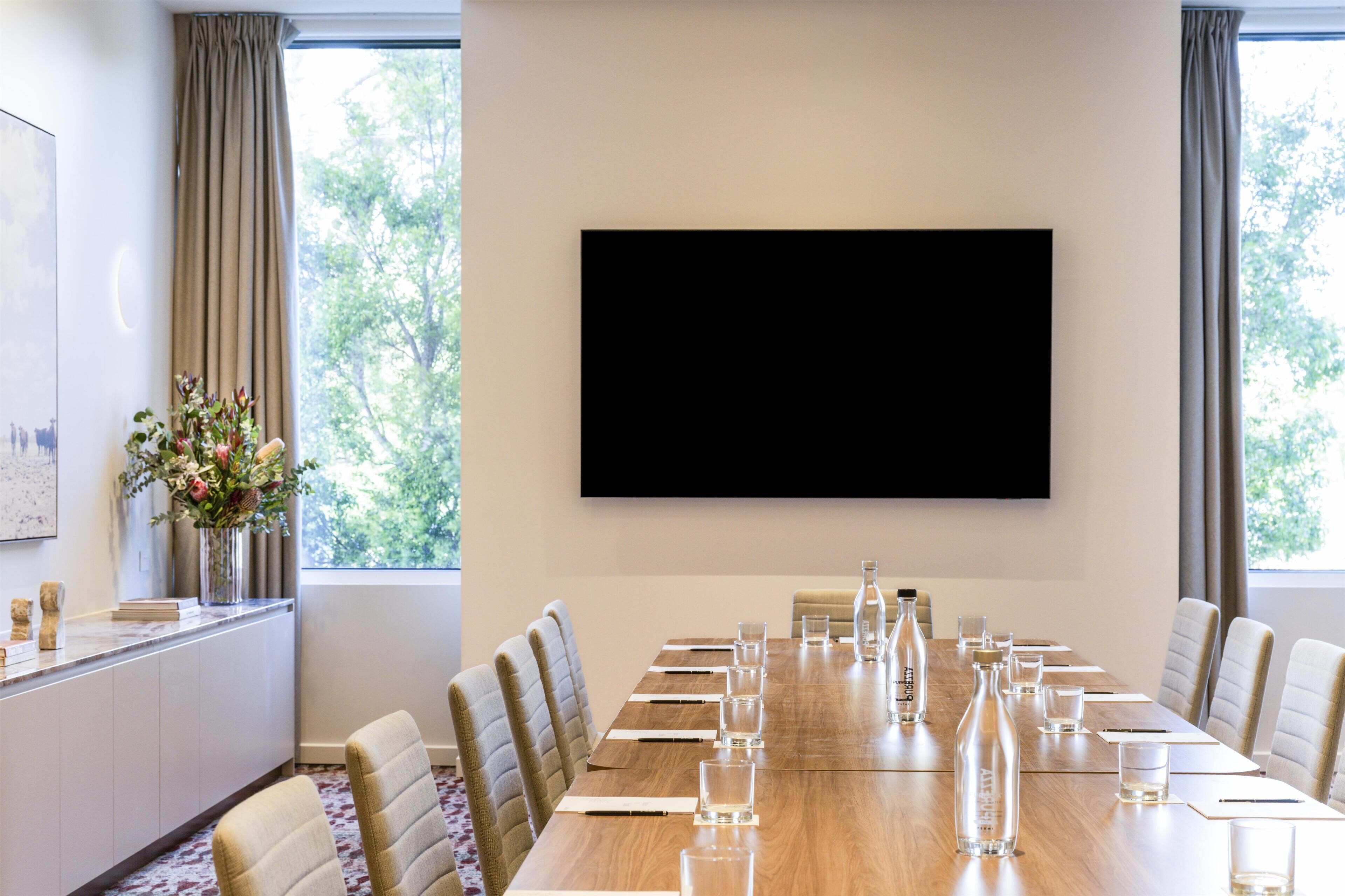 A conference room with a long table, chairs, a flat-screen TV, and a vase of flowers.