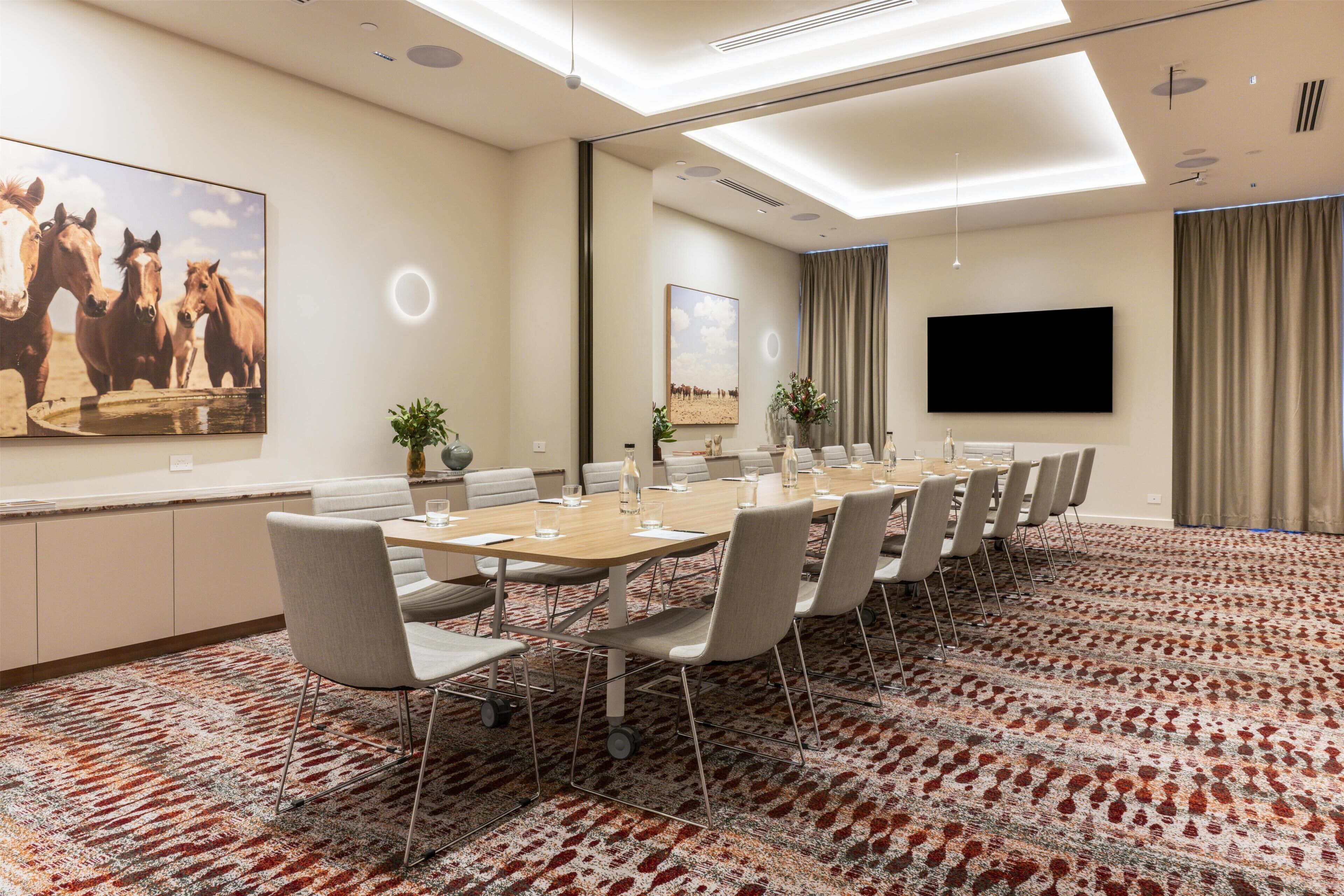 A conference room with a long table, chairs, a flat-screen TV, and a painting of horses.