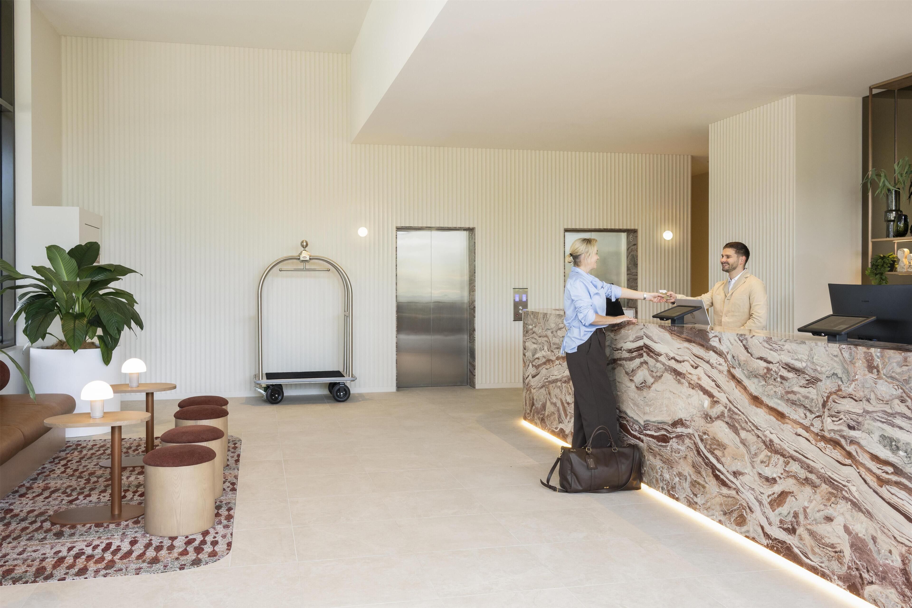 Ein Hotel-Empfangsbereich mit Marmorplatte, einer Rezeption, einem Empfangswagen und einer großen Pflanze in einem Topf.