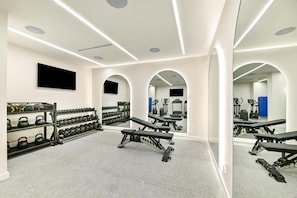 A gym with weightlifting equipment, mirrors, and a television.