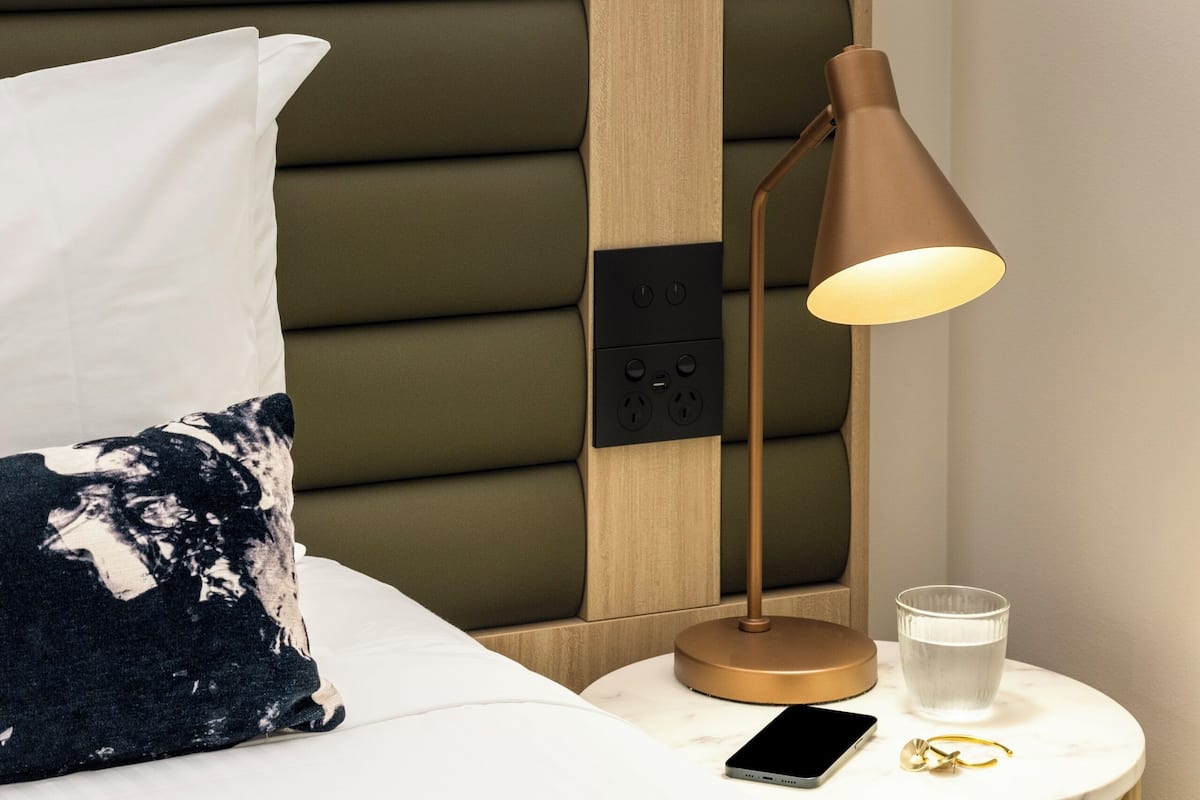 A neatly made bed with a pillow, a bedside lamp, a glass of water, and a smartphone on a bedside table.