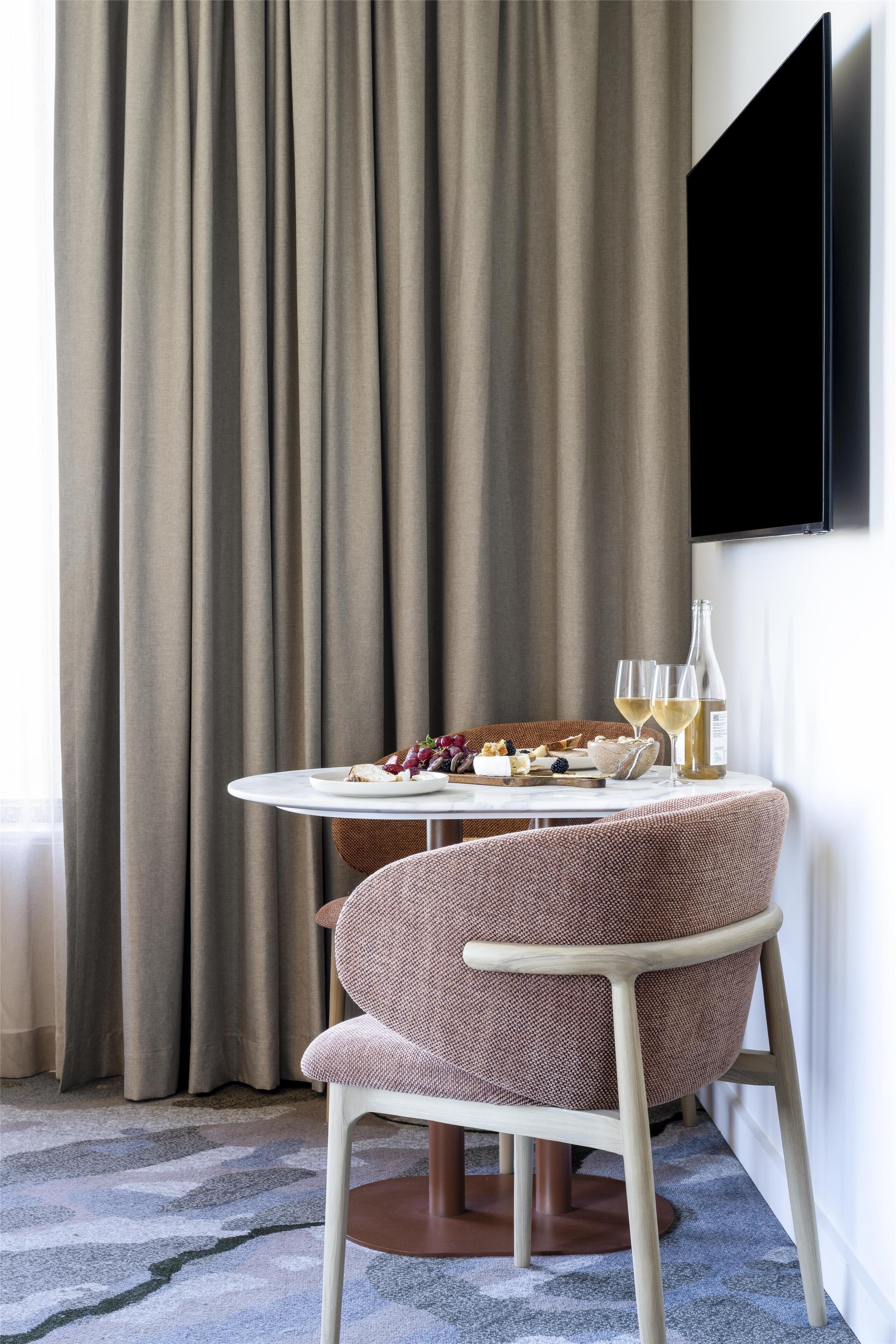 Une pièce avec une table ronde dressée pour deux personnes, une bouteille de vin et une assiette de nourriture.