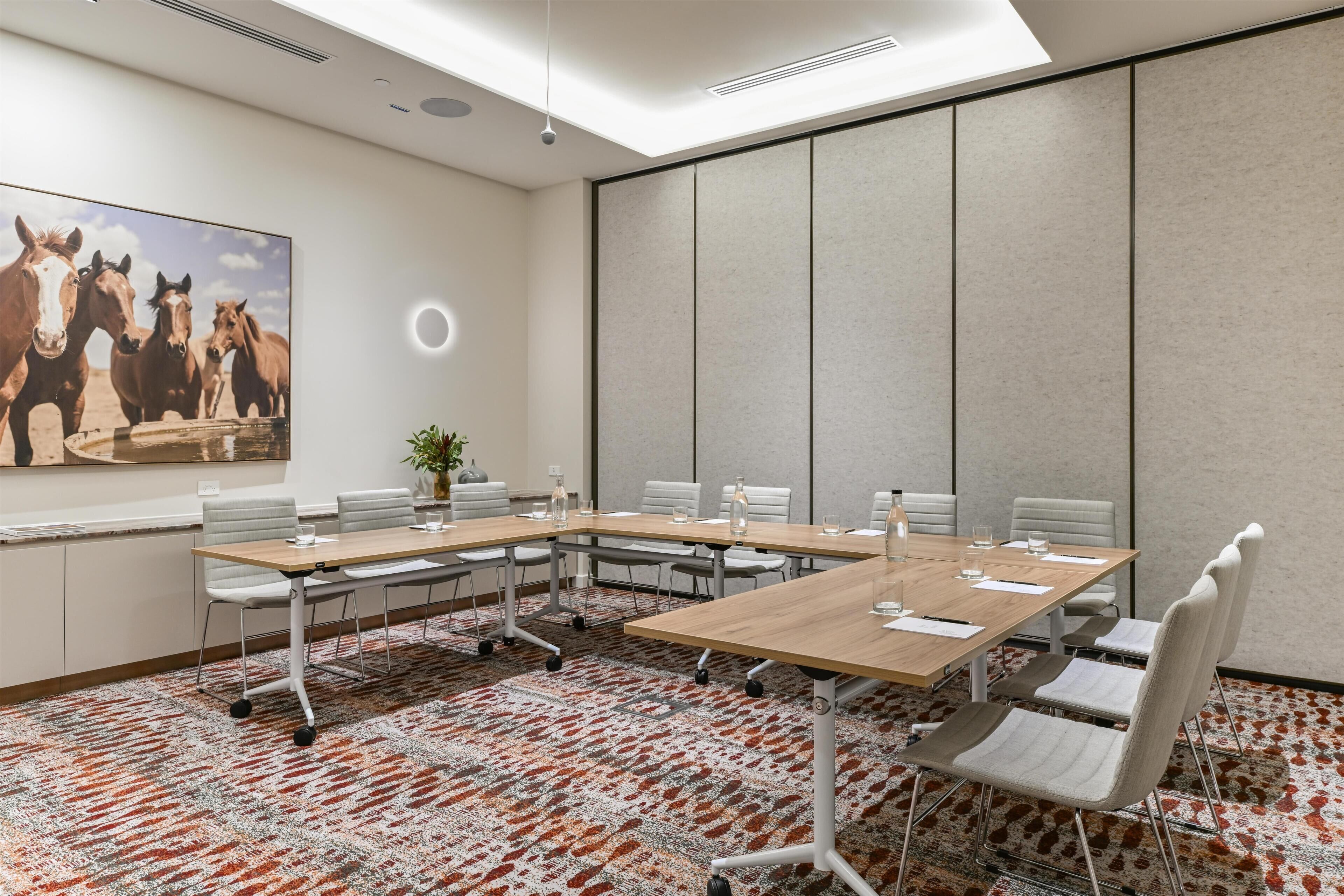 A conference room with a large table, chairs, a plant, and a painting of horses.