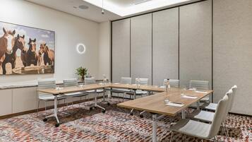 A conference room with a large table, chairs, a plant, and a painting of horses.