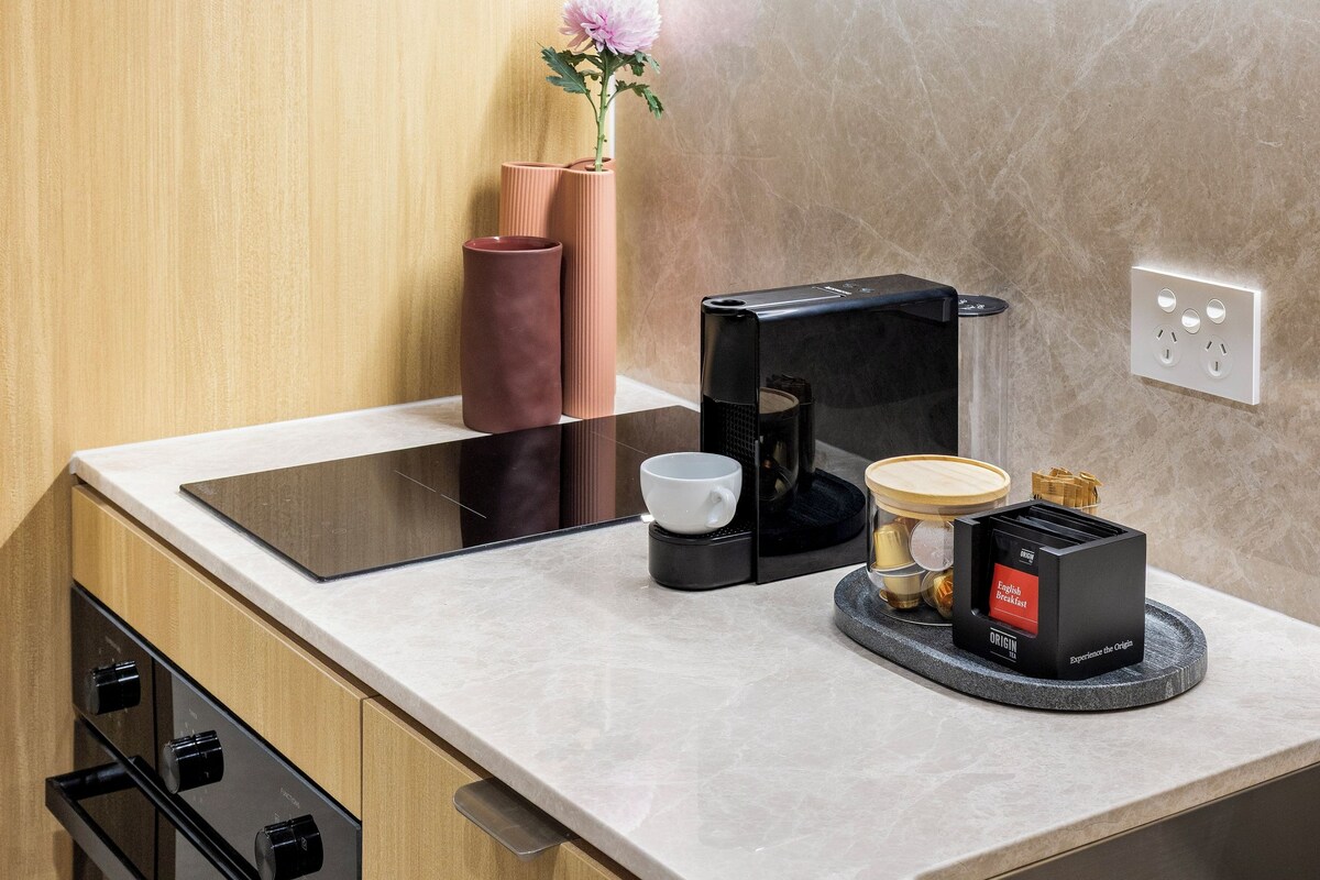 Eine moderne Küche mit Holzausstattung, einer Marmorarbeitsplatte, einem eingebauten Ofen, einer Kaffeemaschine und einer dekorativen Vase mit Blumen.