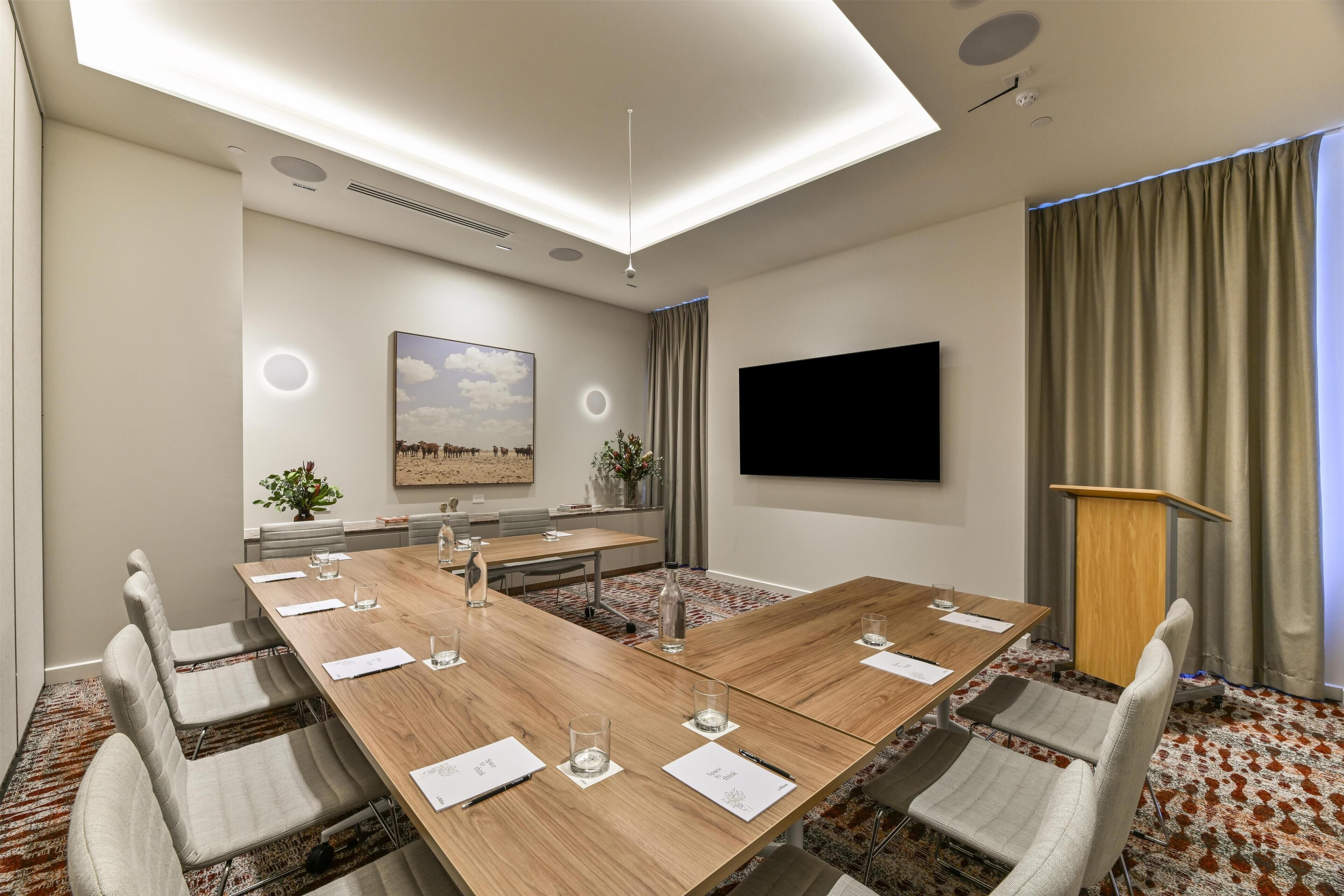 A conference room with a long table, chairs, a TV, and a podium.