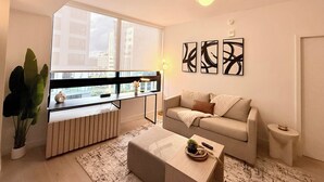 A modern living room with a sofa, a coffee table, a side table, a potted plant, and abstract wall art. - Luxury 1BR Downtown Miami  / Rooftop Pool / Free Parking  / Gym / Work Space (Miami)