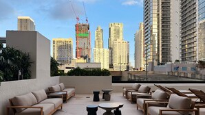 A rooftop terrace with modern furniture, a city skyline view, and a construction crane in the background. - Luxury 1BR Downtown Miami  / Rooftop Pool / Free Parking  / Gym / Work Space (Miami)