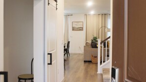Un couloir mène à un espace de vie comprenant un canapé, une lampe et un tableau accroché au mur.