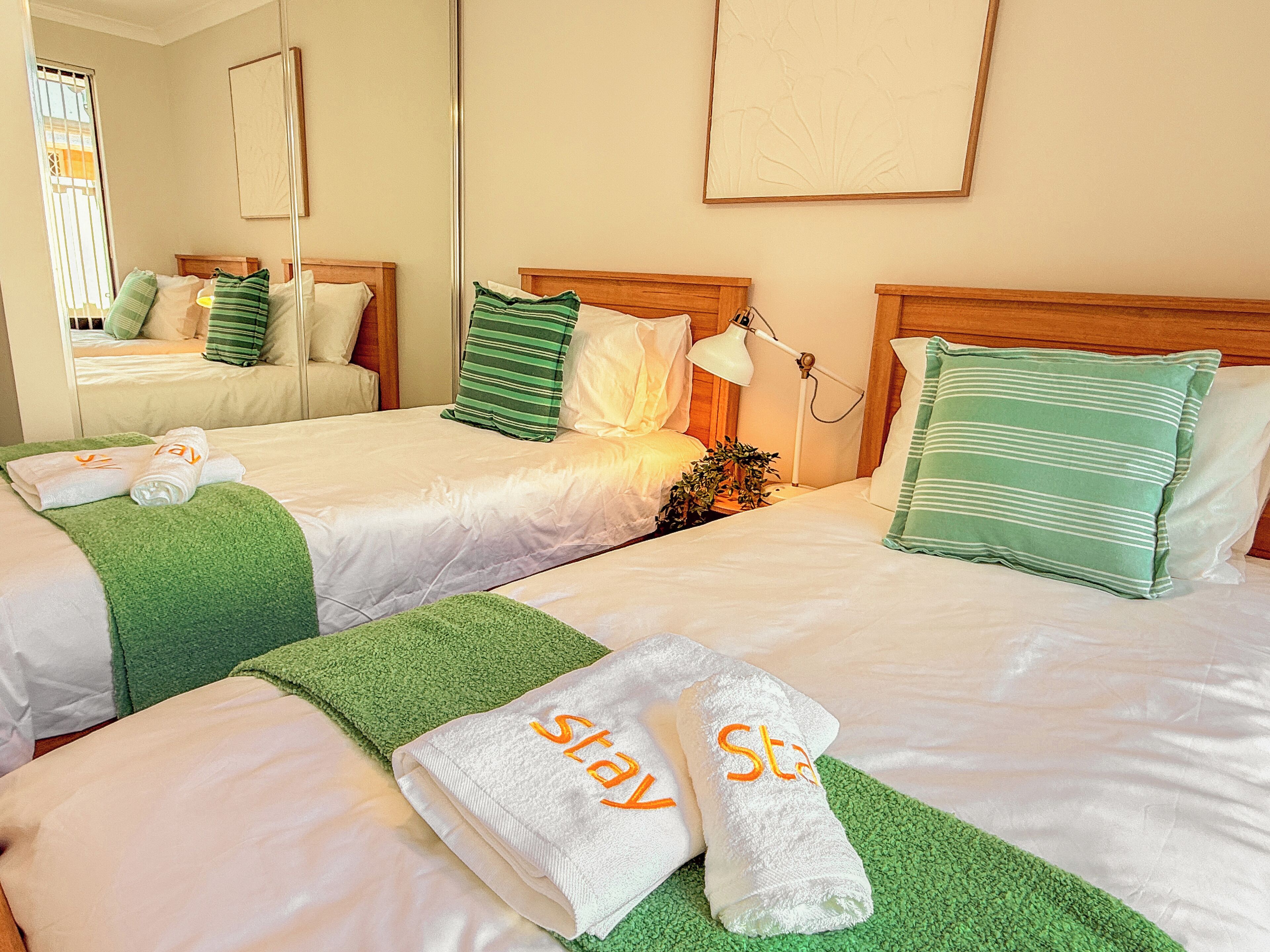 A hotel room with two beds, each with green and white bedding, and towels with 'Stay' embroidered on them.