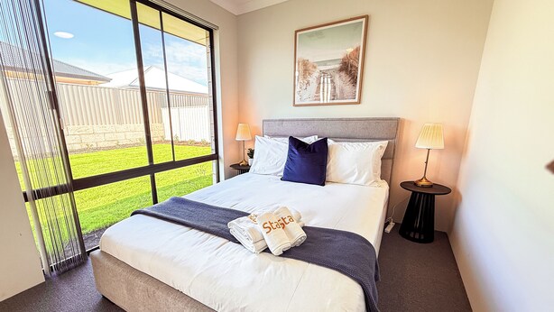 Hotelkamer met een groot bed, twee bedlampen, uitzicht op een grasveld door een schuifdeur en een ingelijst schilderij aan de muur.