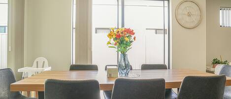 Ein Konferenzraum mit einem Holztisch, sechs Stühlen, einer Blumenvase, einer Uhr und einem Fenster mit Jalousien.