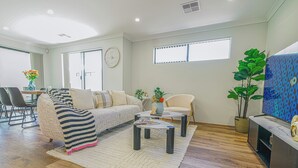 Een moderne woonkamer met een bank, salontafel en stoelen. Er is een eethoek met een tafel en stoelen, en een groot raam zorgt voor natuurlijk licht.