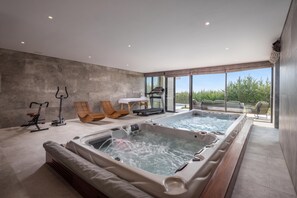 Uma área moderna de piscina interna com duas banheiras de hidromassagem, equipamentos de ginástica e assentos.