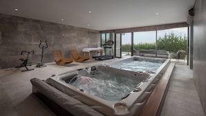 Een moderne spa-ruimte met twee whirlpools, trainingsapparatuur en uitzicht op de omgeving.