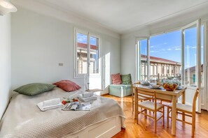 A bedroom with a bed, a table with chairs, and a window with a view of buildings. - Appartamento Villa Mary - Sea View & Balcony, Sanremo, Italy (Sanremo)