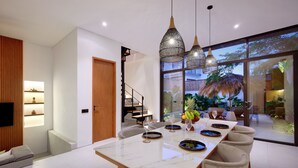 Une cuisine moderne dotée d’un grand îlot central, de luminaires suspendus et offrant une vue sur le jardin extérieur.