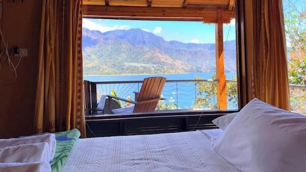 A room with a bed, a chair, and a view of mountains and a lake. - Lily's House, entire cabin in San Juan La Laguna (Solola)
