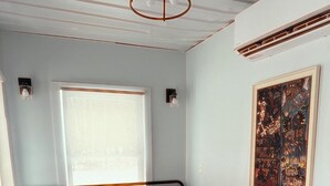A bed with a red and gold bedspread, a window with blinds, and a framed artwork on the wall.