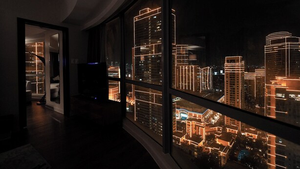 A modern hotel room with a large window overlooking a cityscape at night. - The Hotel Residences at Aqua - Premier Suite  (Mandaluyong City)