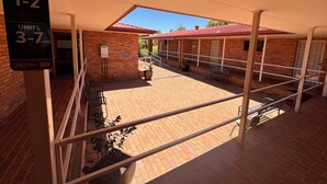 Un espace extérieur abrité, doté d’un sol en briques, de rampes en métal et d’un panneau indiquant les numéros des salles communes 1 à 2 et 3 à 7.