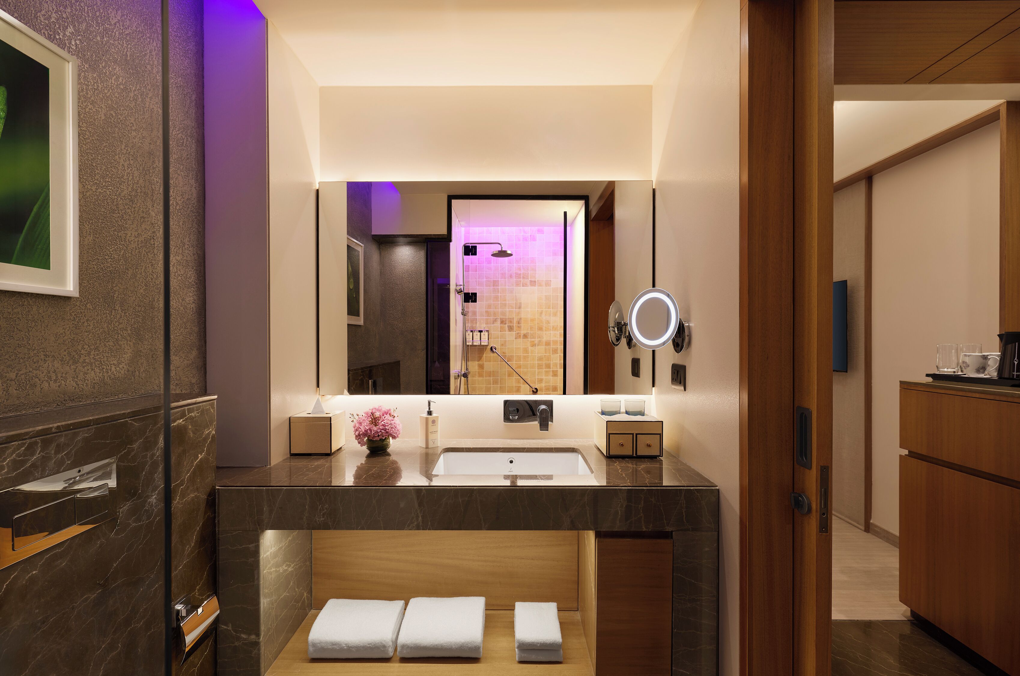 Une salle de bain moderne avec un meuble-lavabo en marbre, un grand miroir et une zone de douche visible à travers la porte en verre.