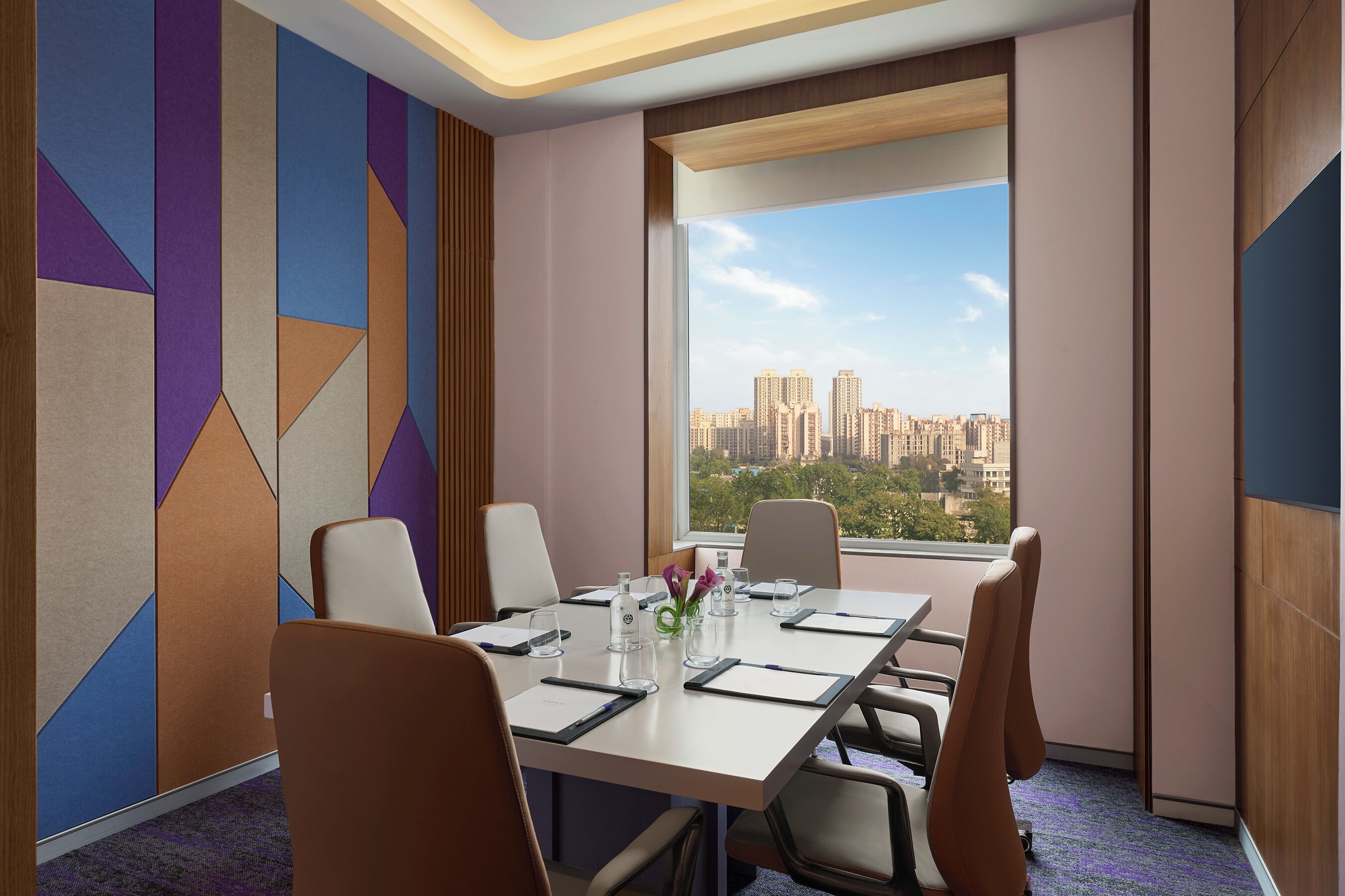 A conference room with a city view, a table with chairs, and a decorative wall.
