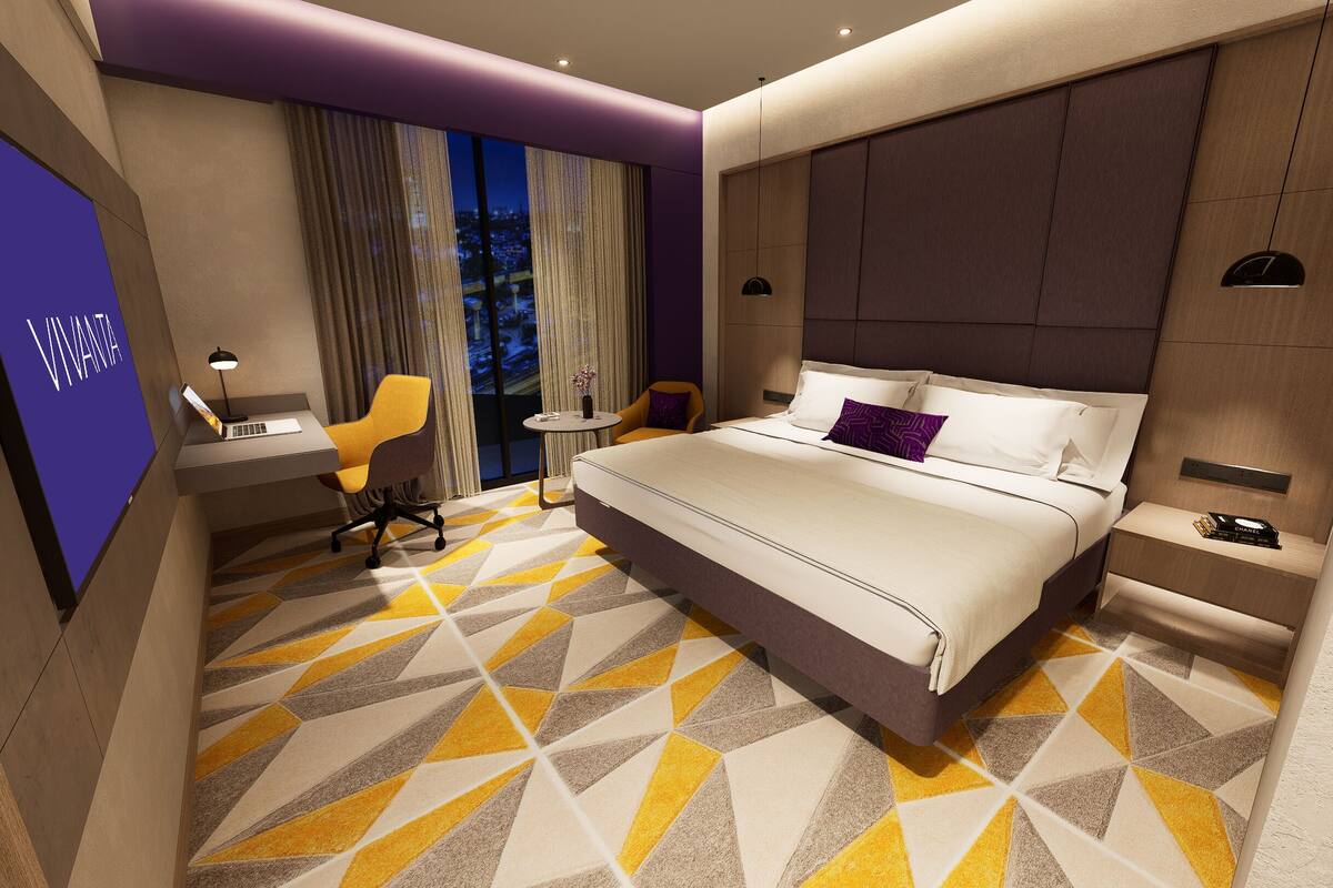 Une chambre d’hôtel moderne, dotée d’un grand lit, d’un bureau, d’une chaise et offrant une vue sur la ville la nuit.